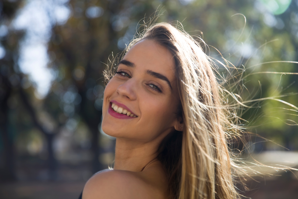 Young Woman with Natural Smile, Cosmetic Dentistry in Scotts Valley, CA Young woman with a bright, natural smile outdoors on a sunny day, representing cosmetic dentistry patients at Mt. Hermon Dental Care in Scotts Valley