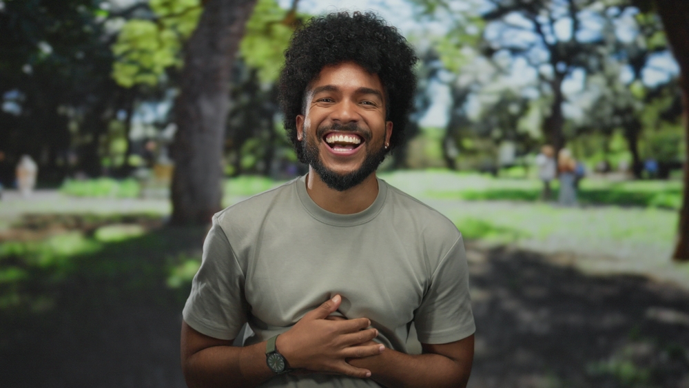 Quality Dental Care in Scotts Valley, CA Young man laughing joyfully outdoors in a park, representing the confidence that comes from quality dental care in the Scotts Valley community