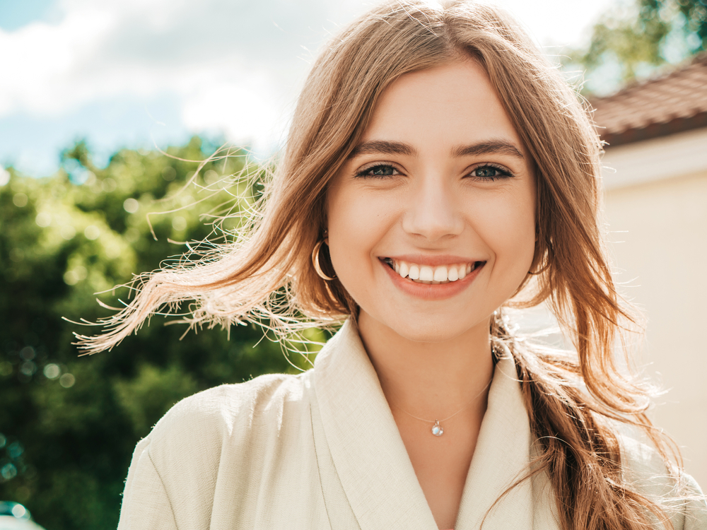 Cosmetic Dentistry and Teeth Whitening in Scotts Valley, CA Young woman with a radiant white smile outdoors on a sunny day, representing cosmetic dental care and teeth whitening at Mt. Hermon Dental Care in Scotts Valley