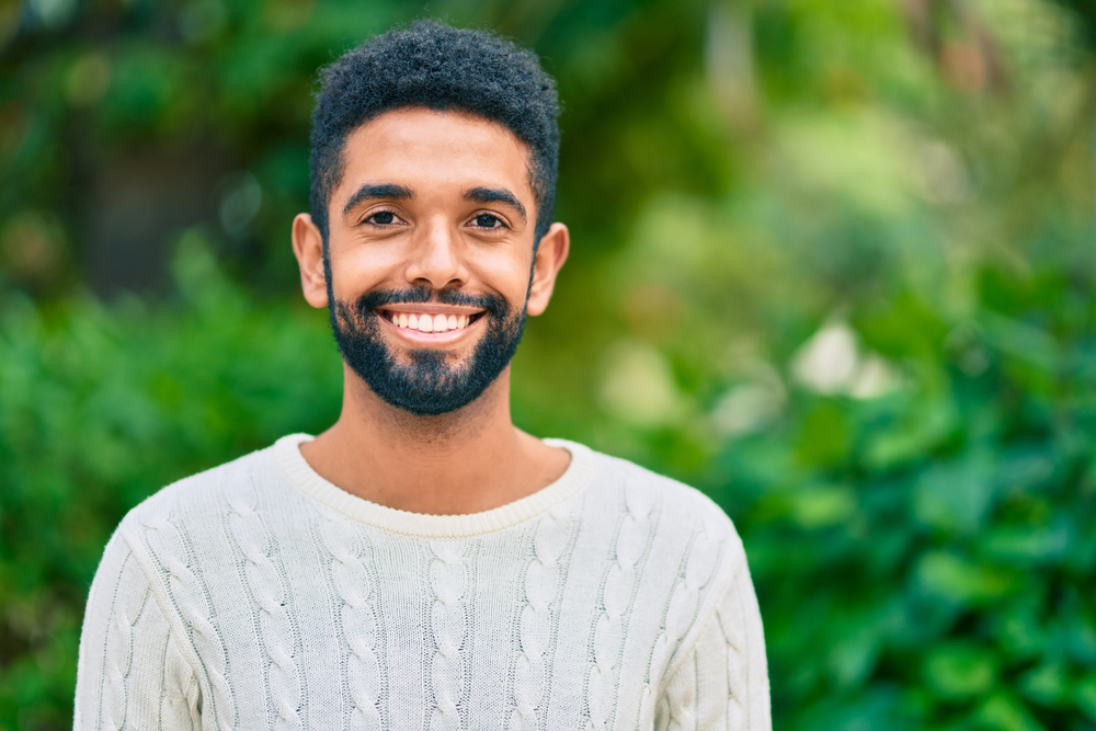Patient with Healthy Smile, General Dentistry Near Scotts Valley, CA Young man with a bright, confident smile outdoors with lush green foliage, representing patients served near Scotts Valley, CA